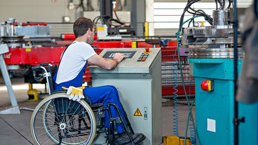 Ein Rollstuhlfahrer arbeitet an einer Maschine. | Bild: stock.adobe.com/Firma V