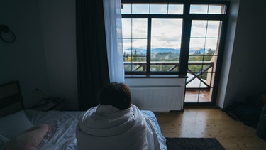 Young woman wrapped in a blanket staring into the distance | Bild: Picture Alliance  / Zoonar / Oleksii