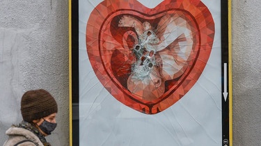 Eine Frau geht an einer zerstörten Werbetafel mit dem Bild eines Fötus in einer herzförmigen Gebärmutter vorbei. | Bild: picture alliance / NurPhoto | Artur Widak